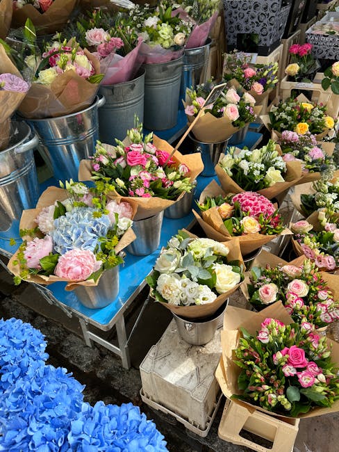 A vibrant display of freshly arranged flower bouquets and potted plants at a flower market, featuring a variety of pastel pink, white, and lavender roses, hydrangeas, and other seasonal blossoms wrapp